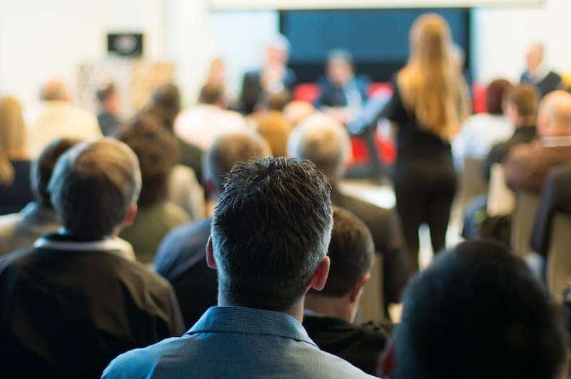 A crowd of people sit in a town hall meeting, showing the Catholic Church and politics at work