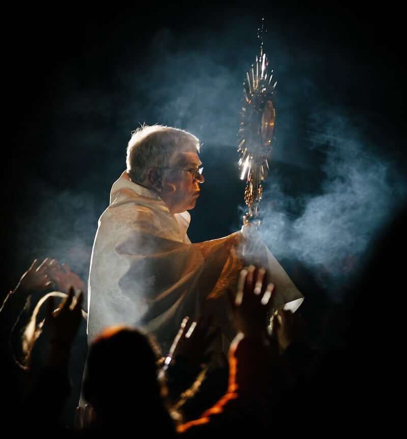 A priest carries the Holy Eucharist in a monstrance amid a cloud of incense and crowd of worshippers, showing that solidarity must flow from faith