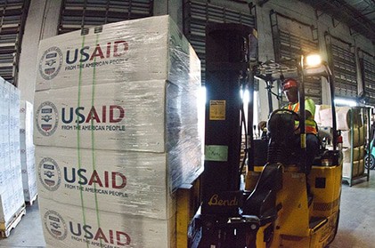 A man drives a forklift carrying US aid packages, showing how the universal destination of goods seeks for created goods to flow fairly to all
