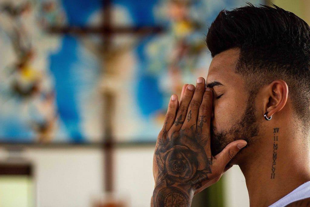 A heavily tattooed man prays in a church, symbolizing the need for personal conversion in order to protect the physical environment