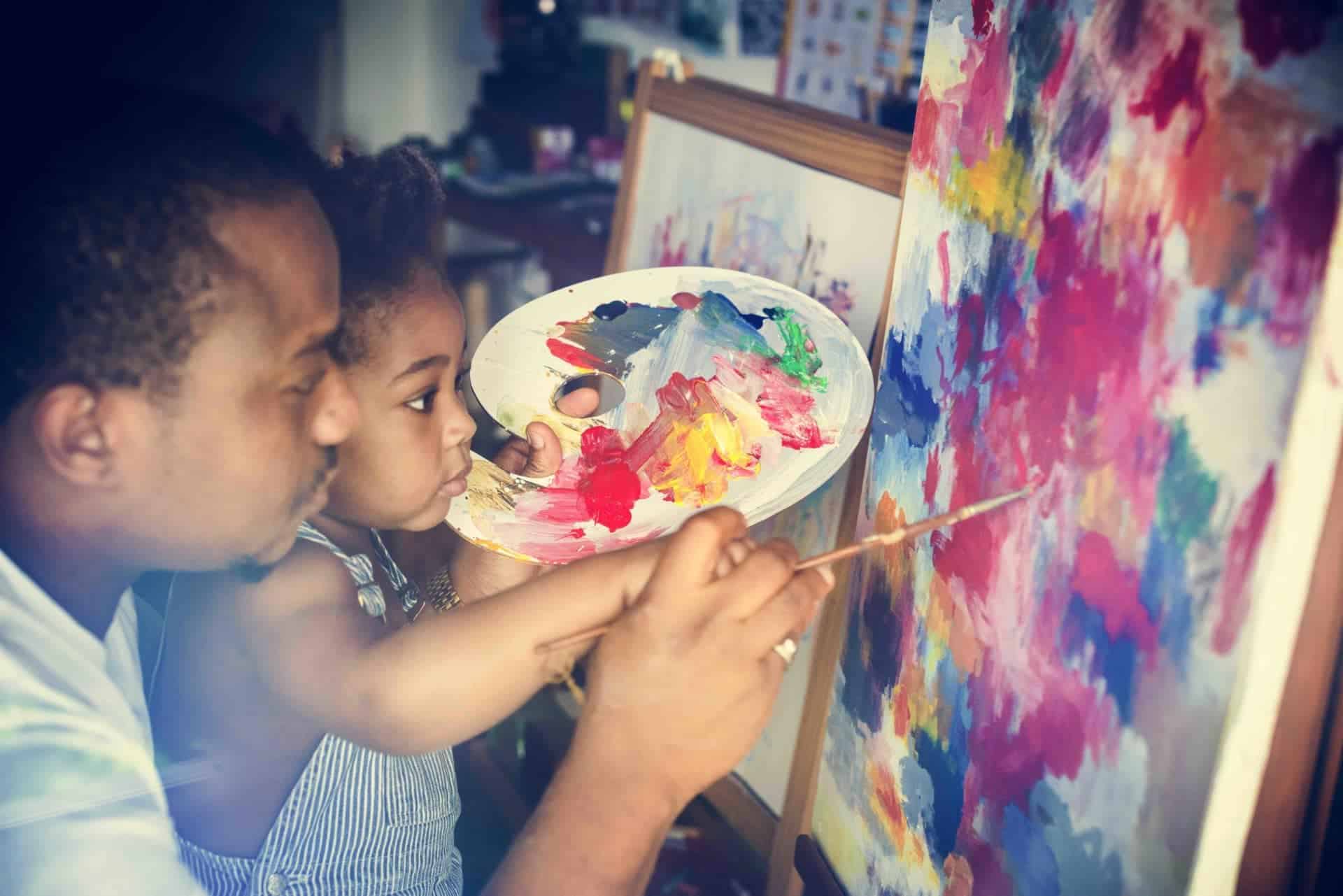 A father helps his toddler with her painting, representing the care that integral ecology requires to be focused upon the human person