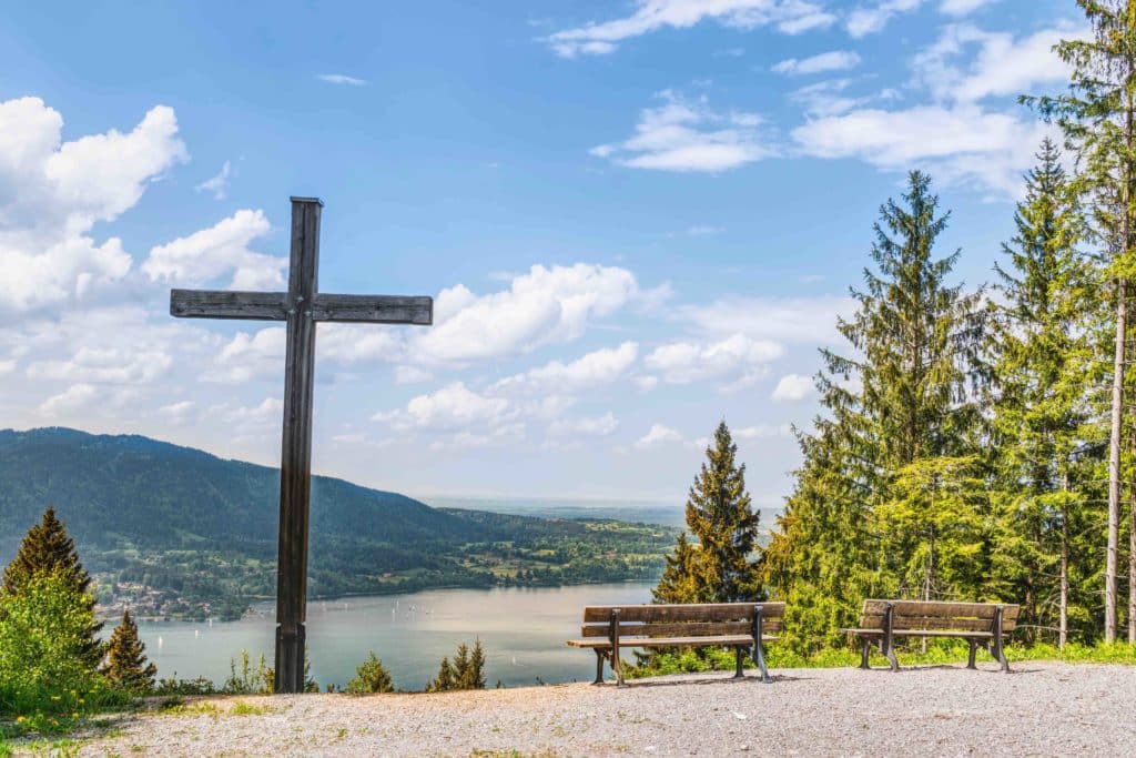 A large cross stands near two benches on the edge of a lake. Faith must play a part in our attitude toward climate change