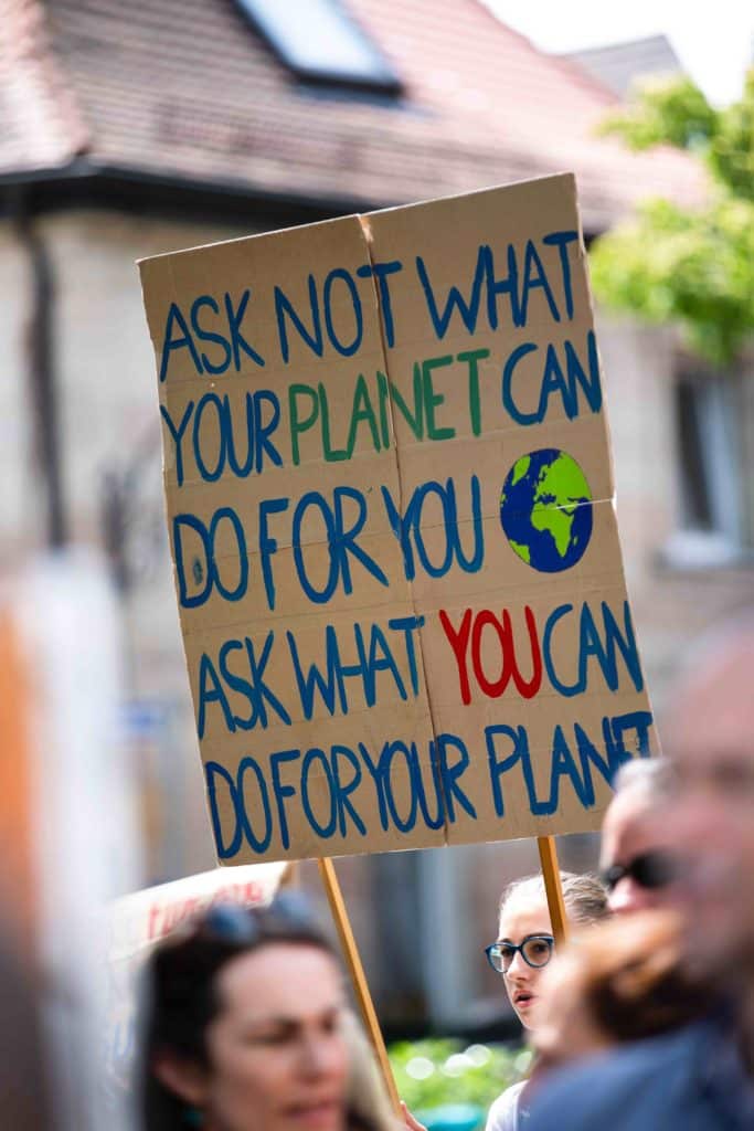 A climate change protester carries a sign saying, "Ask not what your planet can do for you, ask what you can do for your planet"