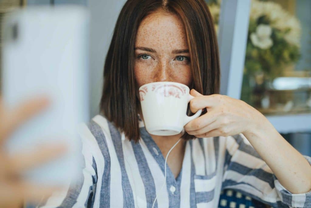 A woman takes a selfie while sipping from a teacup, representing the dangerous individualism which is opposed to integral ecology