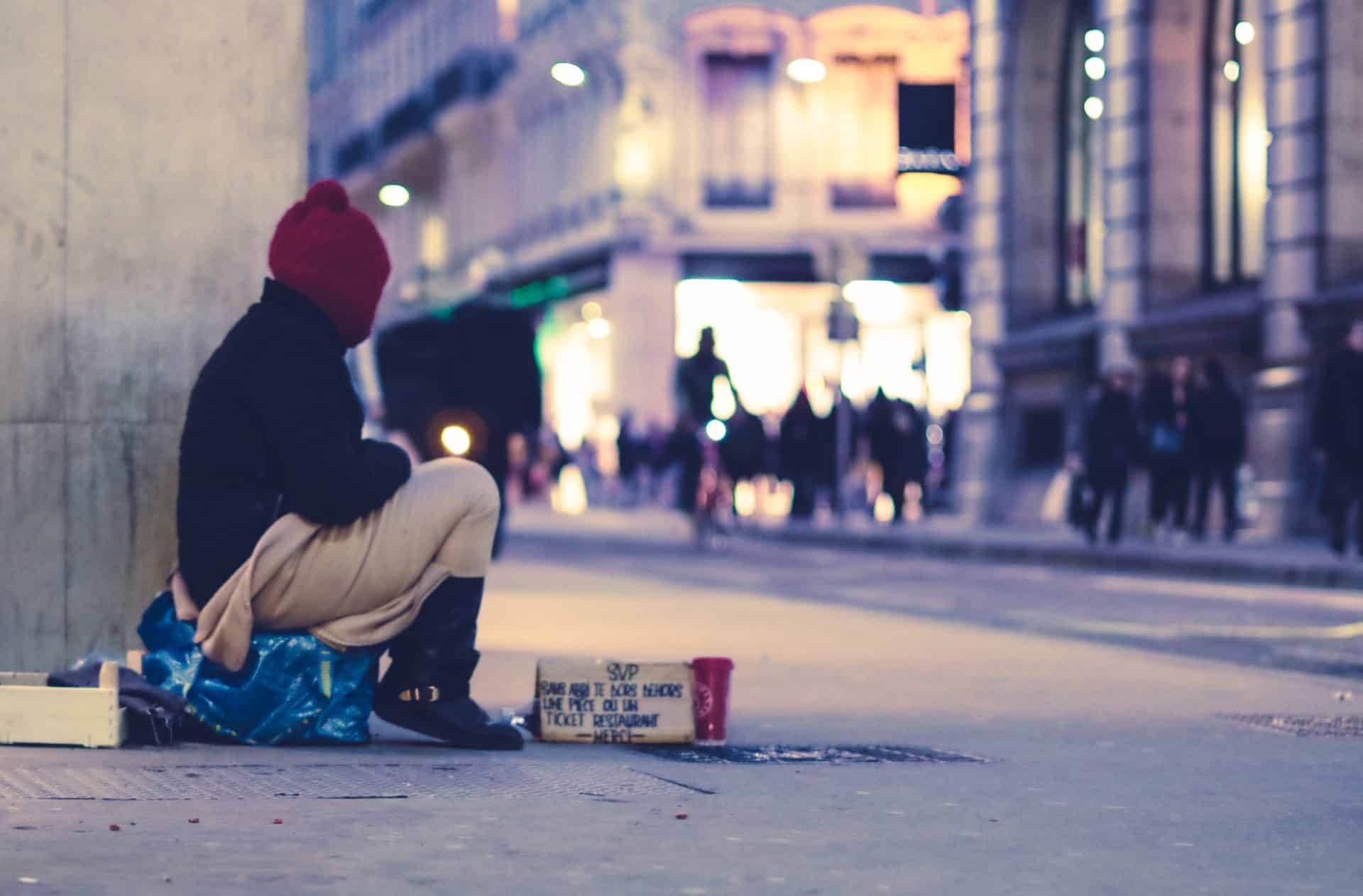 A homeless man sits at the street corner, showing the human need that integral ecology seeks to answer