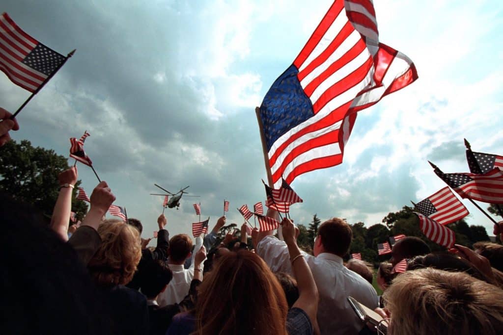 A crowd waves American flags while helicopters fly past, but Catholic social teaching is neither liberal or conservative