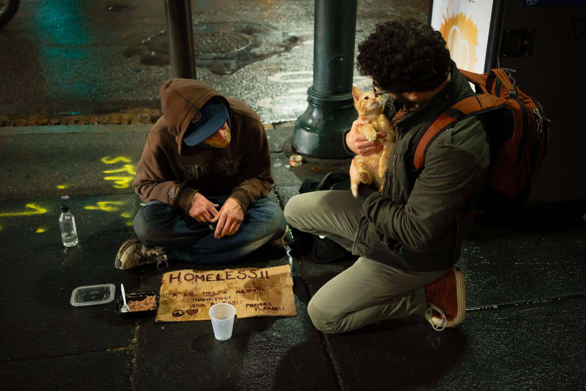 A man with a cat stops to talk with a homeless man, demonstrating that catholic social teaching must confront improper social structures.
