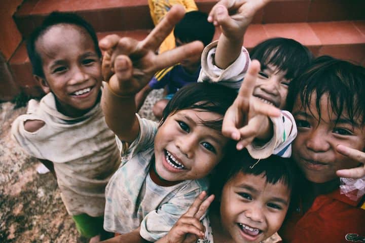 A group of smiling children in poor clothes make the peace sign, suggesting the major themes that Catholic social teaching articles should touch upon