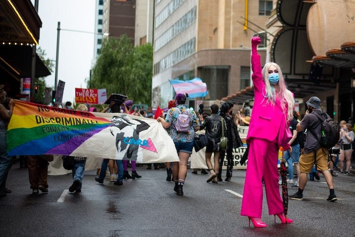 A trans person dressed in pink women's clothing raises a fist during a protest for transgender, gender identity, LGBT rights.