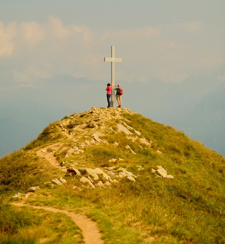 Hikers summit a peak and stand near a large cross Pope Francis calls us to action by remembering that caring for our environment must begin and end in the worship of God.