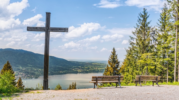 A large cross stands near two benches on the edge of a lake. Faith must play a part in our attitude toward climate change